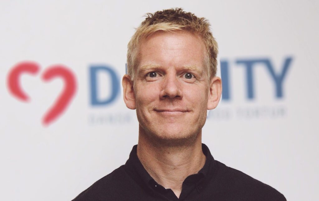 DIGNITY's Direktør der smiler til kameraet foran et DIGNITY banner