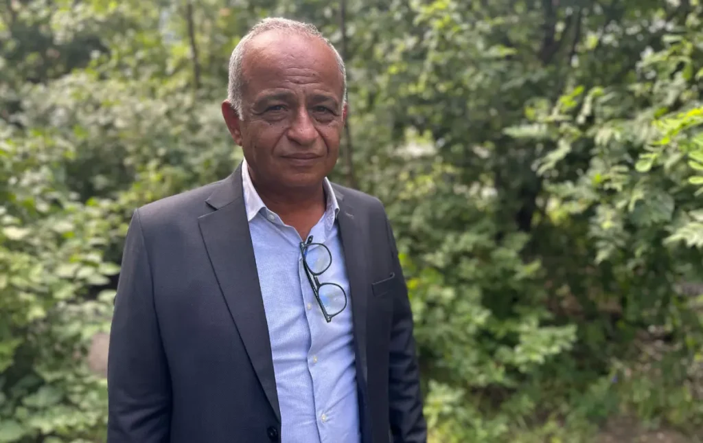 Hamdi Shaqqura in af suit in front of green bushes